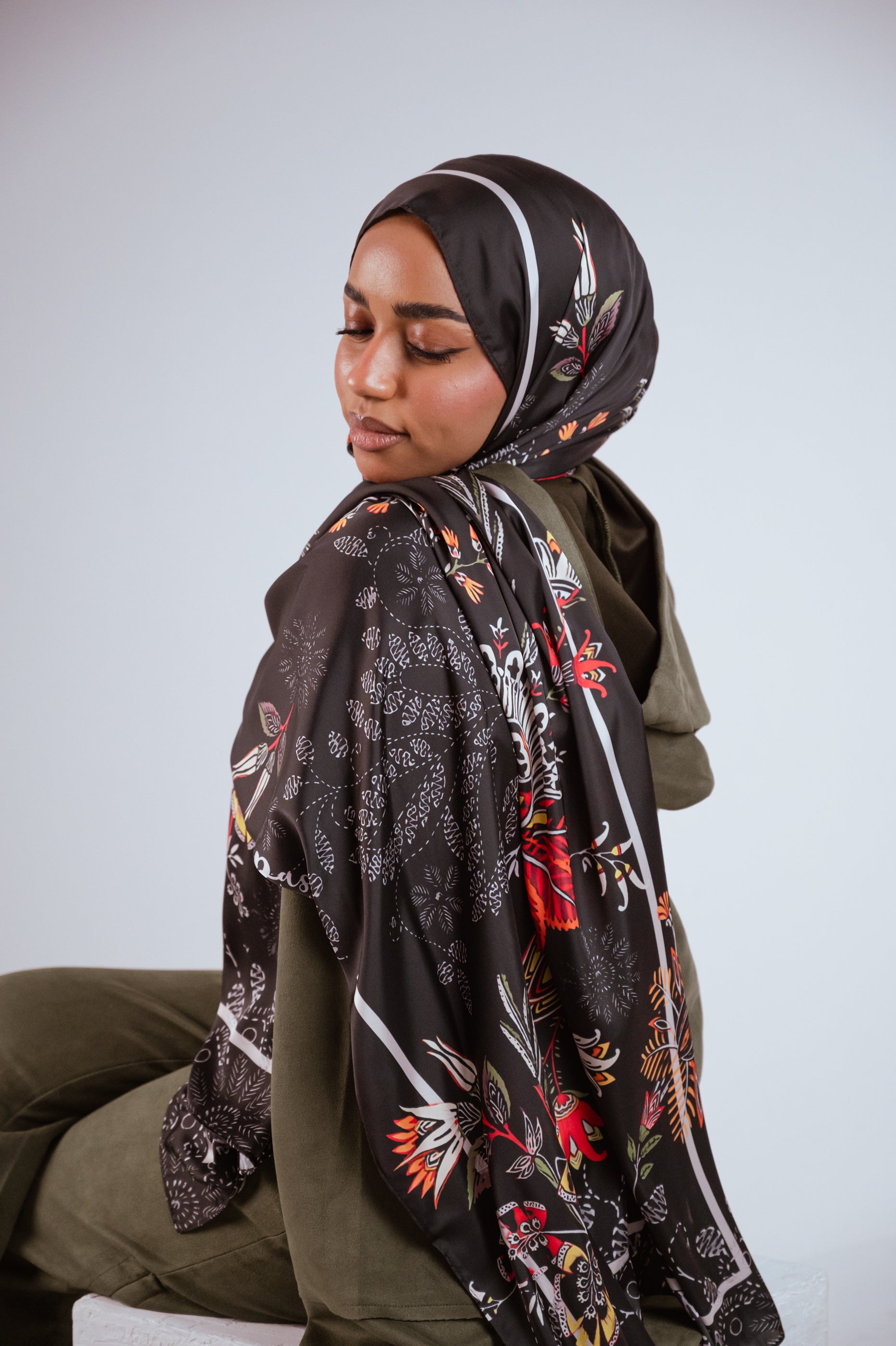 Model in a serene pose wearing the Scarlet of Granada satin hijab, highlighting the deep brown base and colourful floral elements.