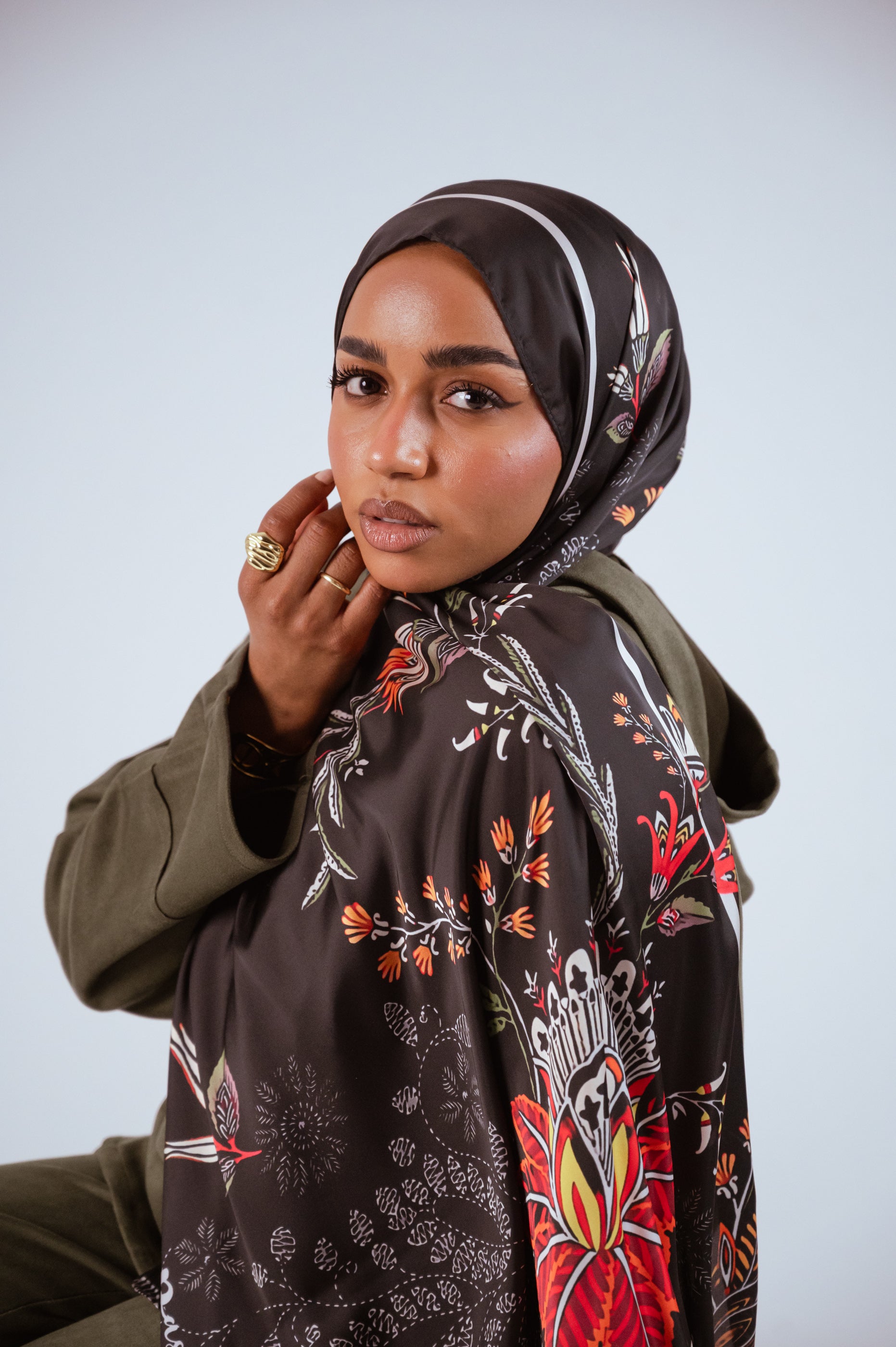 Model seated wearing the Scarlet of Granada satin hijab, displaying the full fall of the satin fabric and floral artwork.