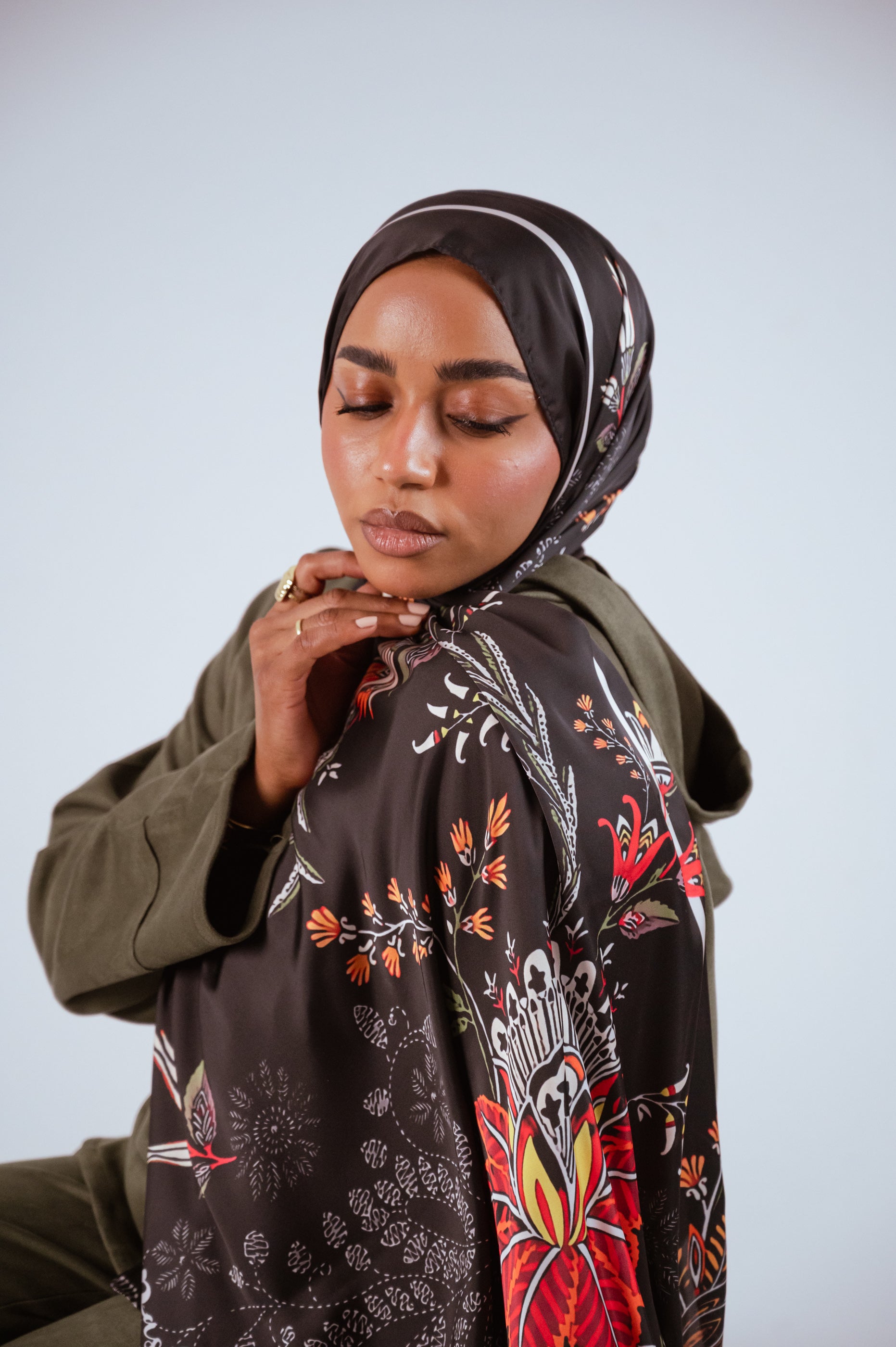 Model with hand near face wearing the Scarlet of Granada satin hijab, emphasizing the soft satin finish and intricate print.