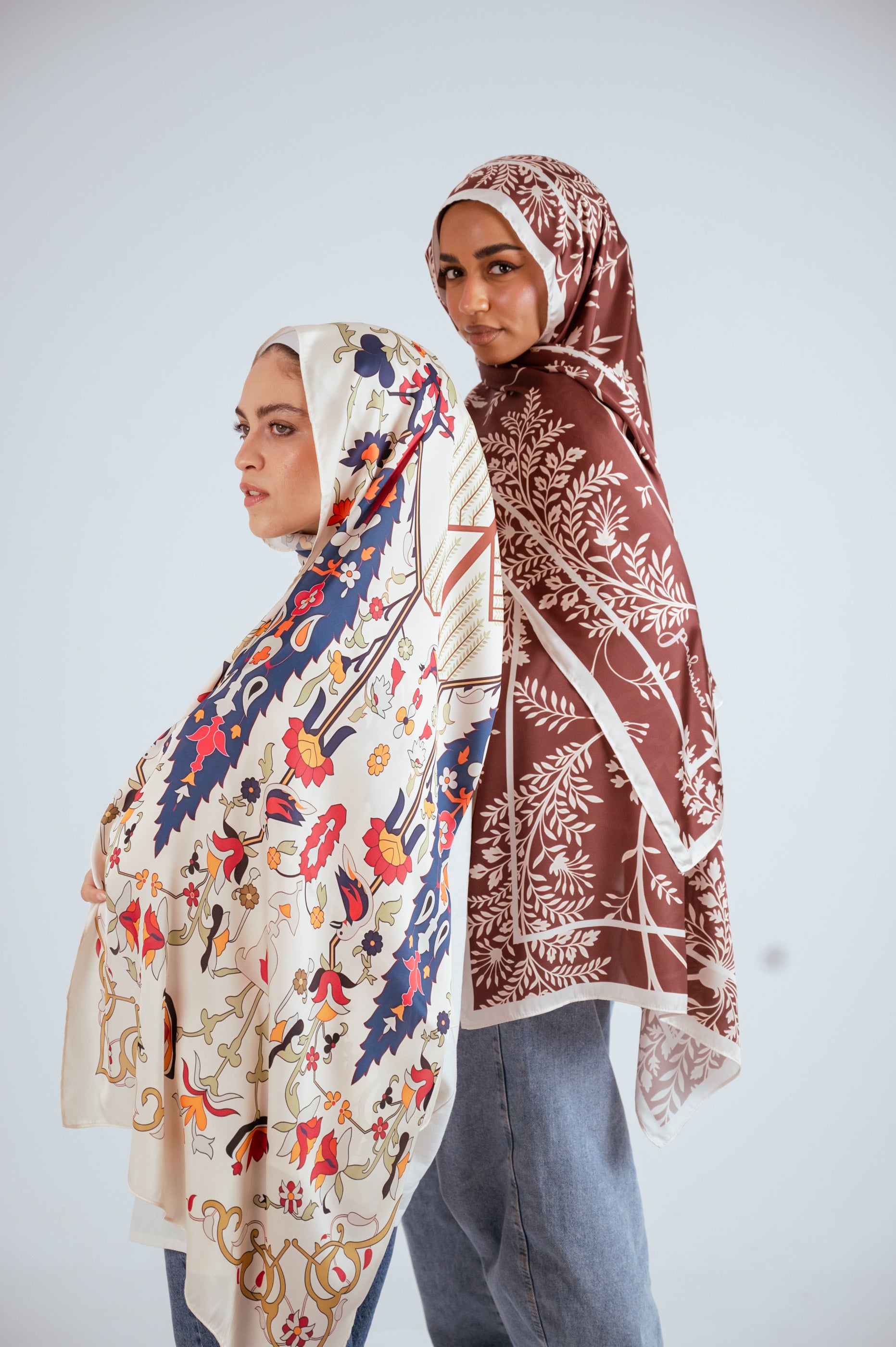 Two models styled in Jaida’s printed satin hijabs, Andalus Drape and Rose of Petra, in neutral and brown tones.