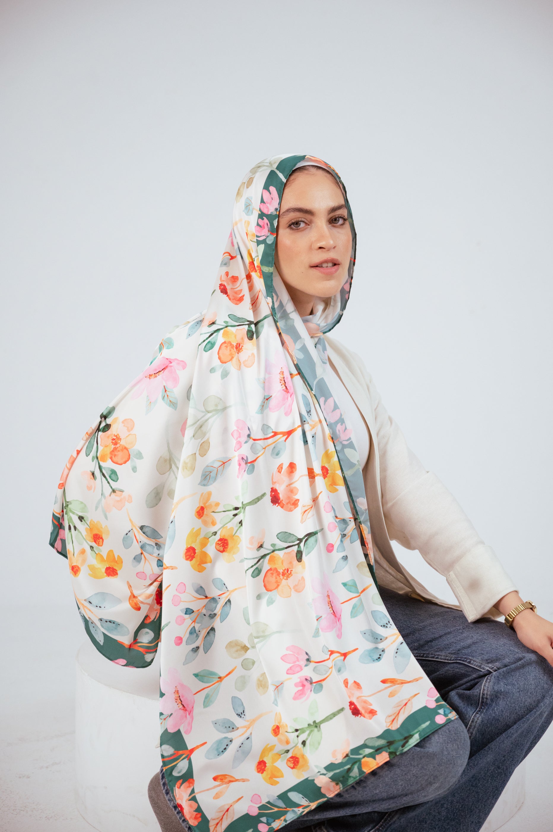 Model seated wearing Blooms of Hope – Luxury Satin Hijab flowing over one side, showing soft satin drape.