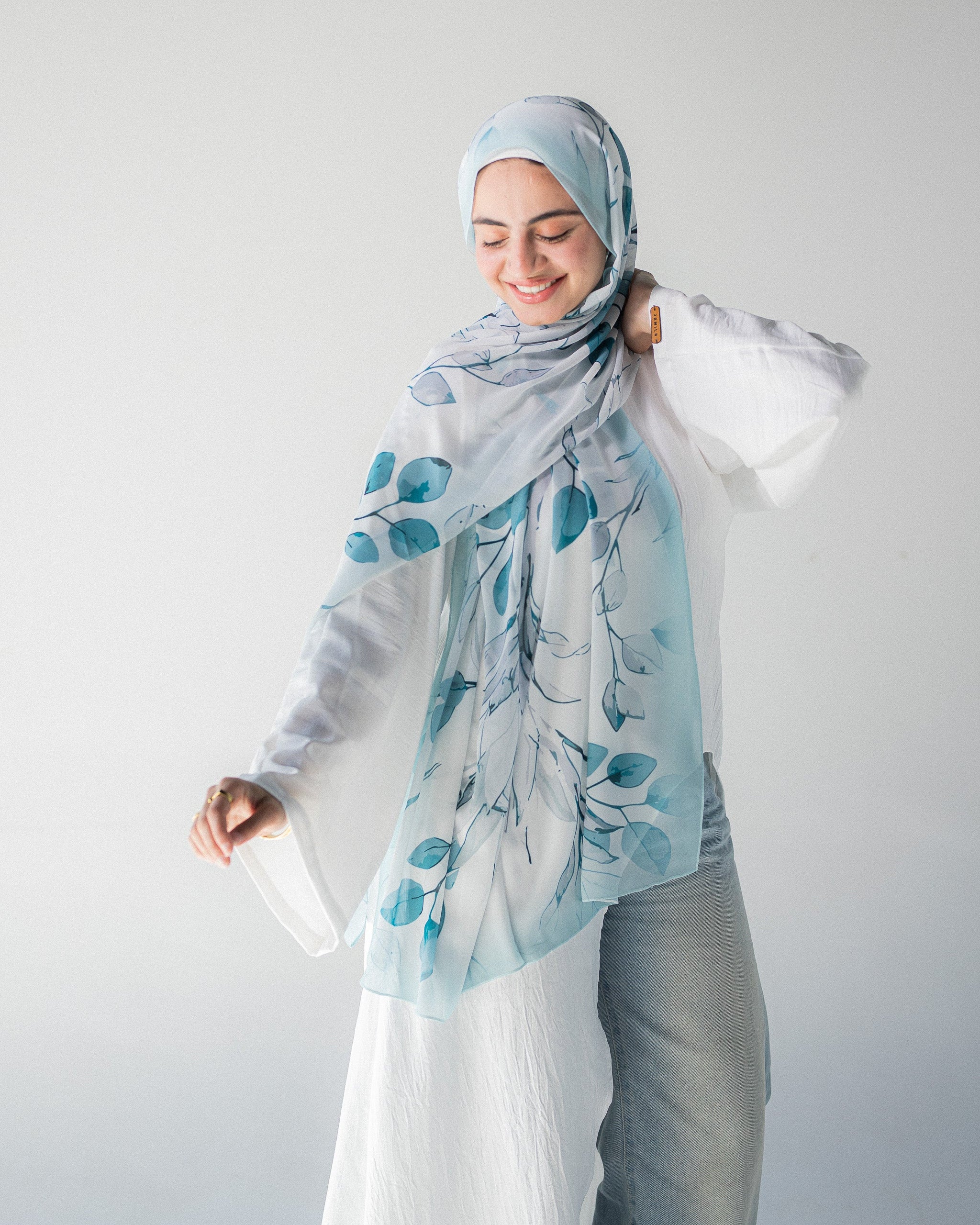 Modest Muslim young woman wearing a light blue hijab with floral patterns on a plain background