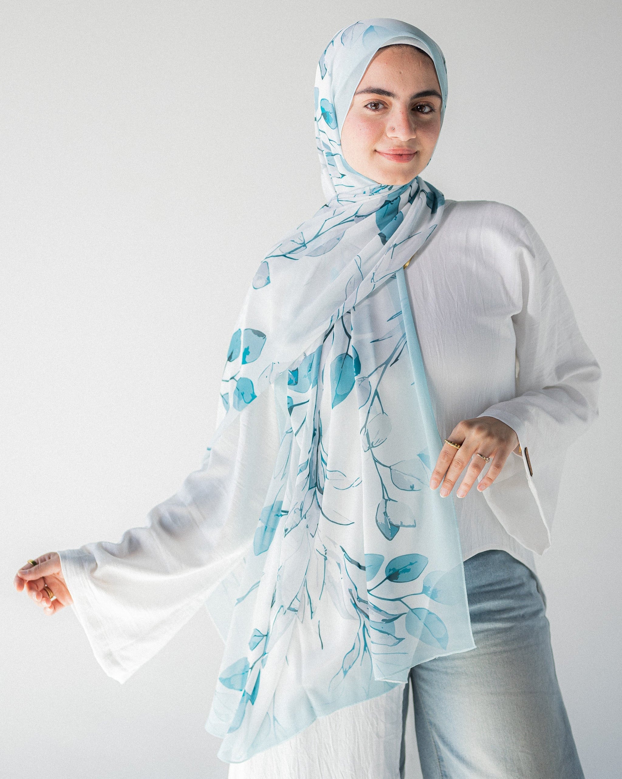 Modest Muslim young woman wearing a light blue hijab with floral patterns on a plain background