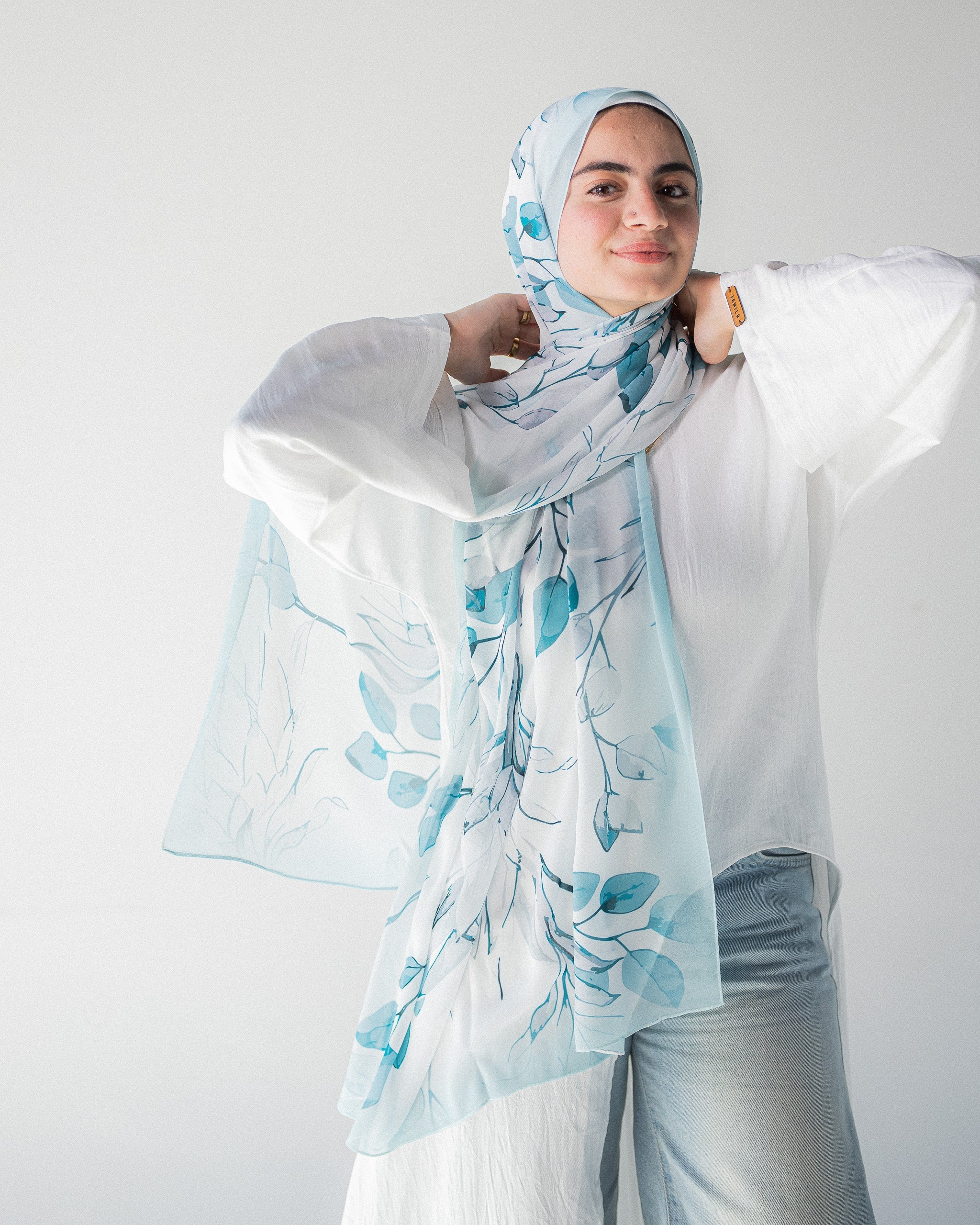 Modest Muslim young woman wearing a light blue hijab with floral patterns on a plain background
