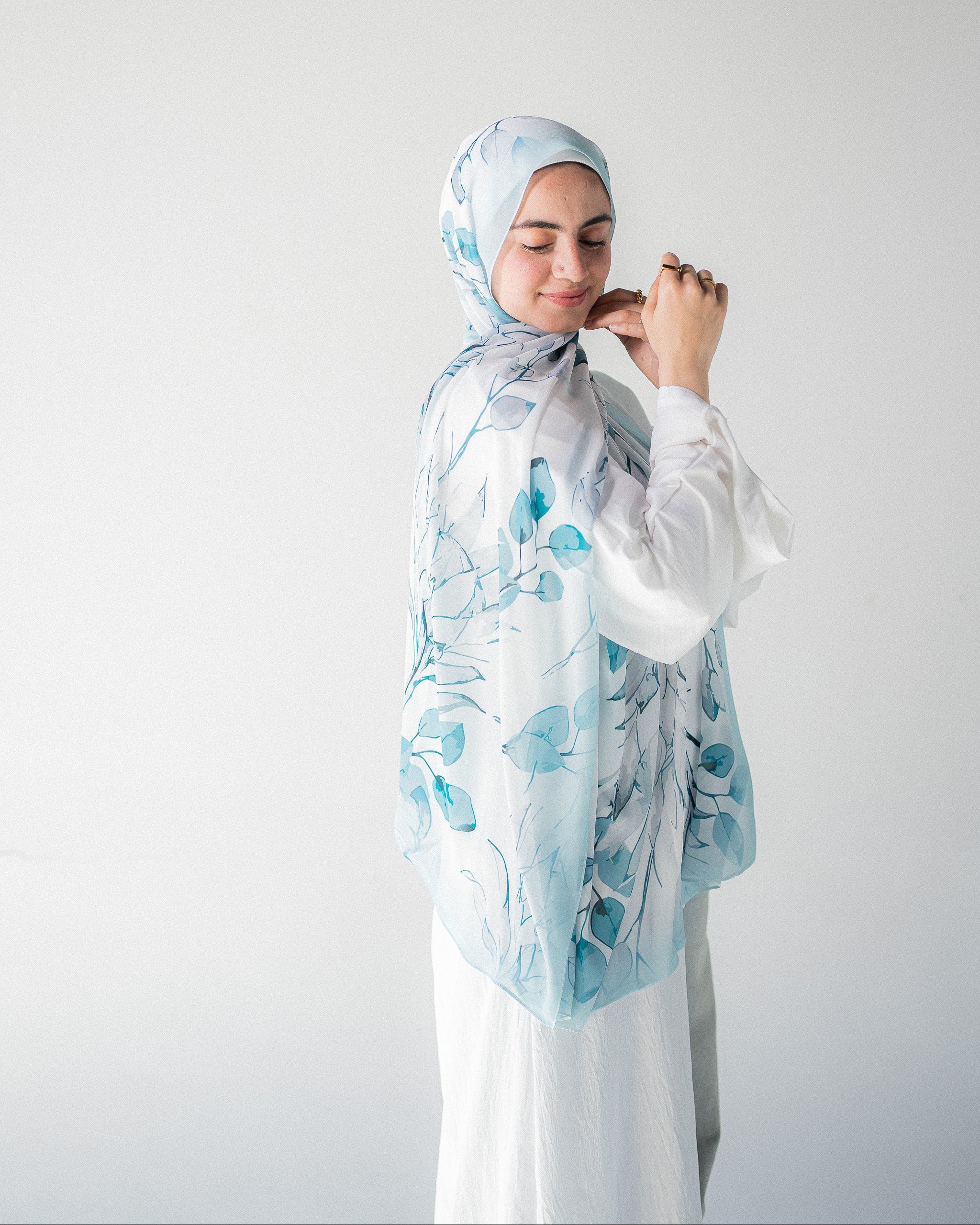 Modest Muslim young woman wearing a light blue hijab with floral patterns on a plain background
