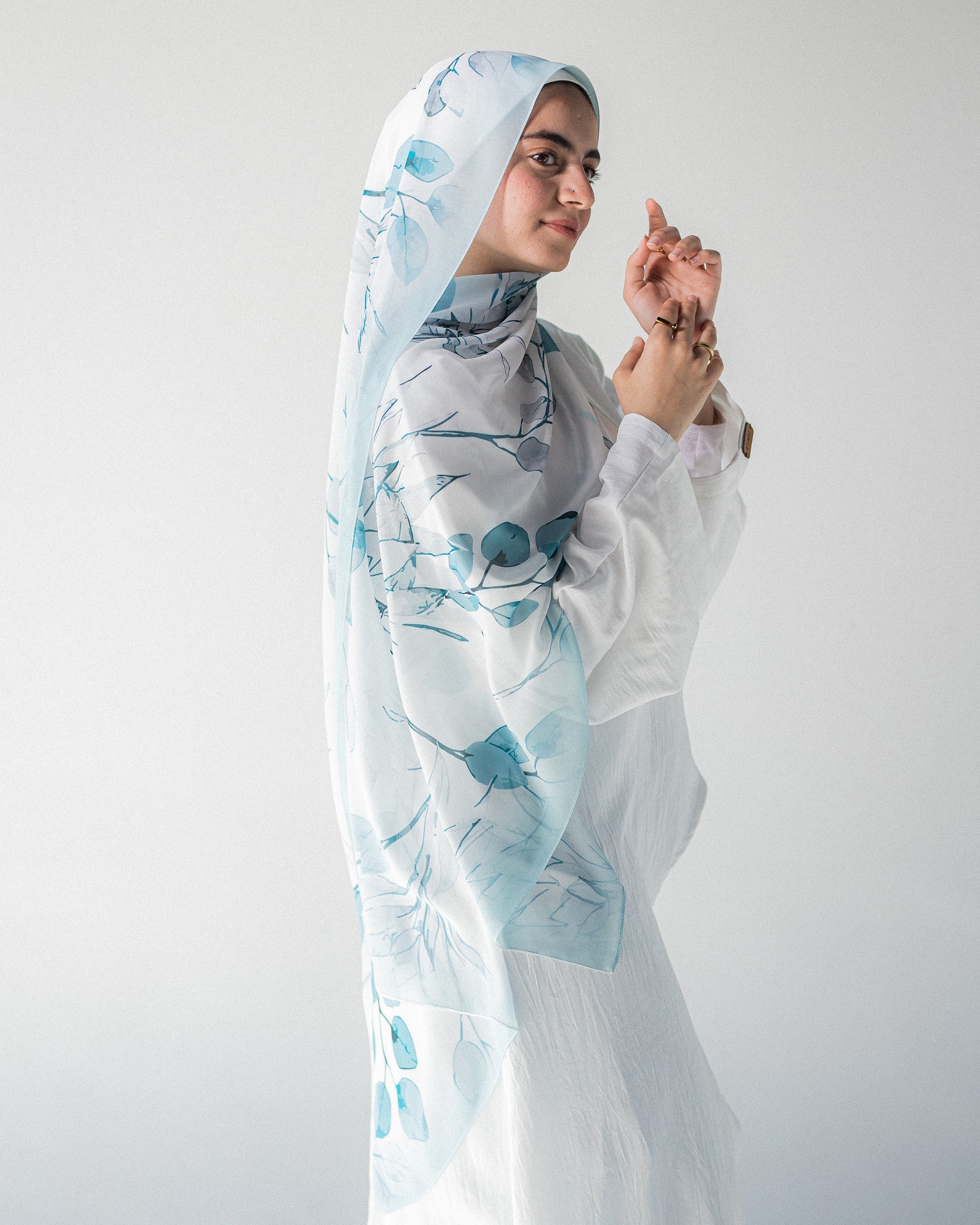 Modest Muslim young woman wearing a light blue hijab with floral patterns on a plain background