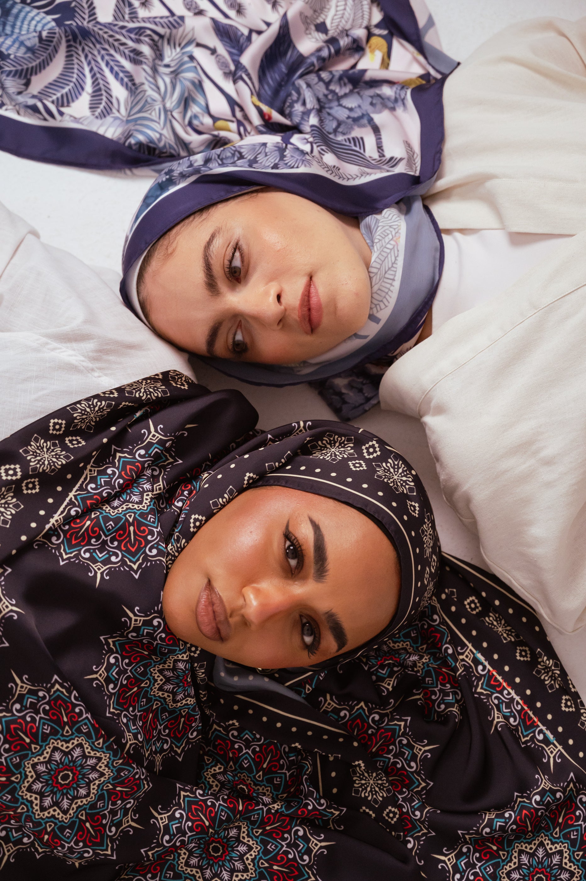 Two models lying side by side wearing Blooms of Hope and Andalusia Satin Hijabs from JAIDA.