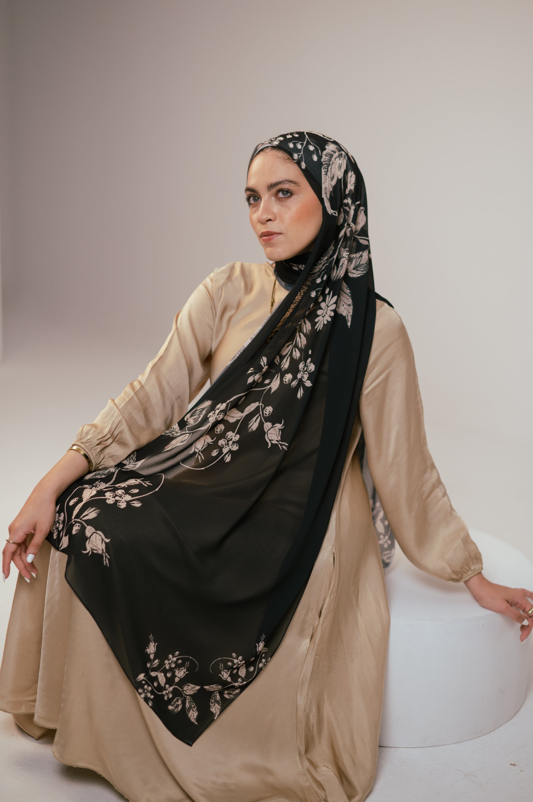 Petal Shadows chiffon hijab styled in a seated pose, with the floral design displayed across the lap.