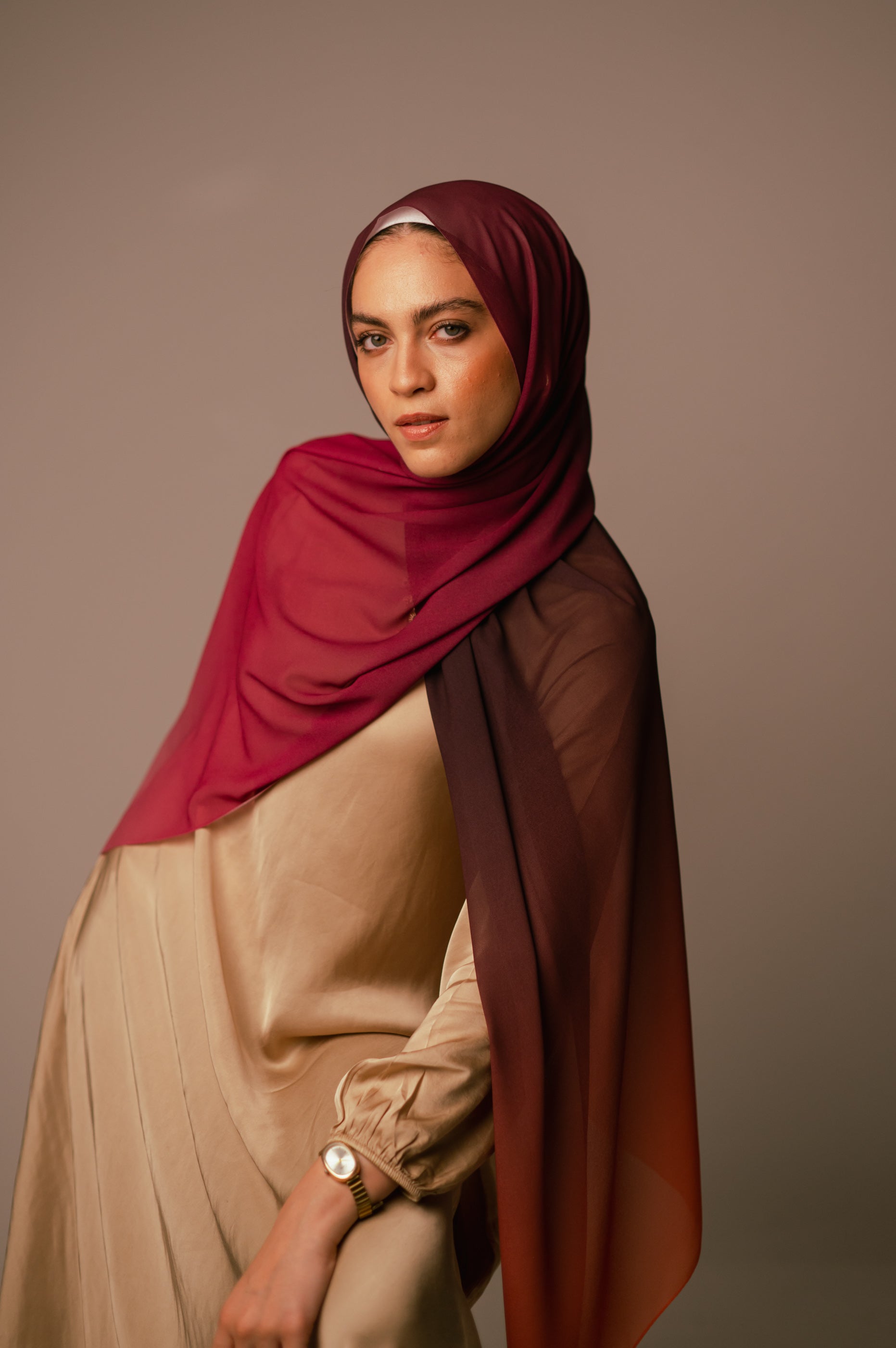 Model posing seated, wearing the Wisteria Sunset chiffon hijab with soft pink-to-plum gradient drape.