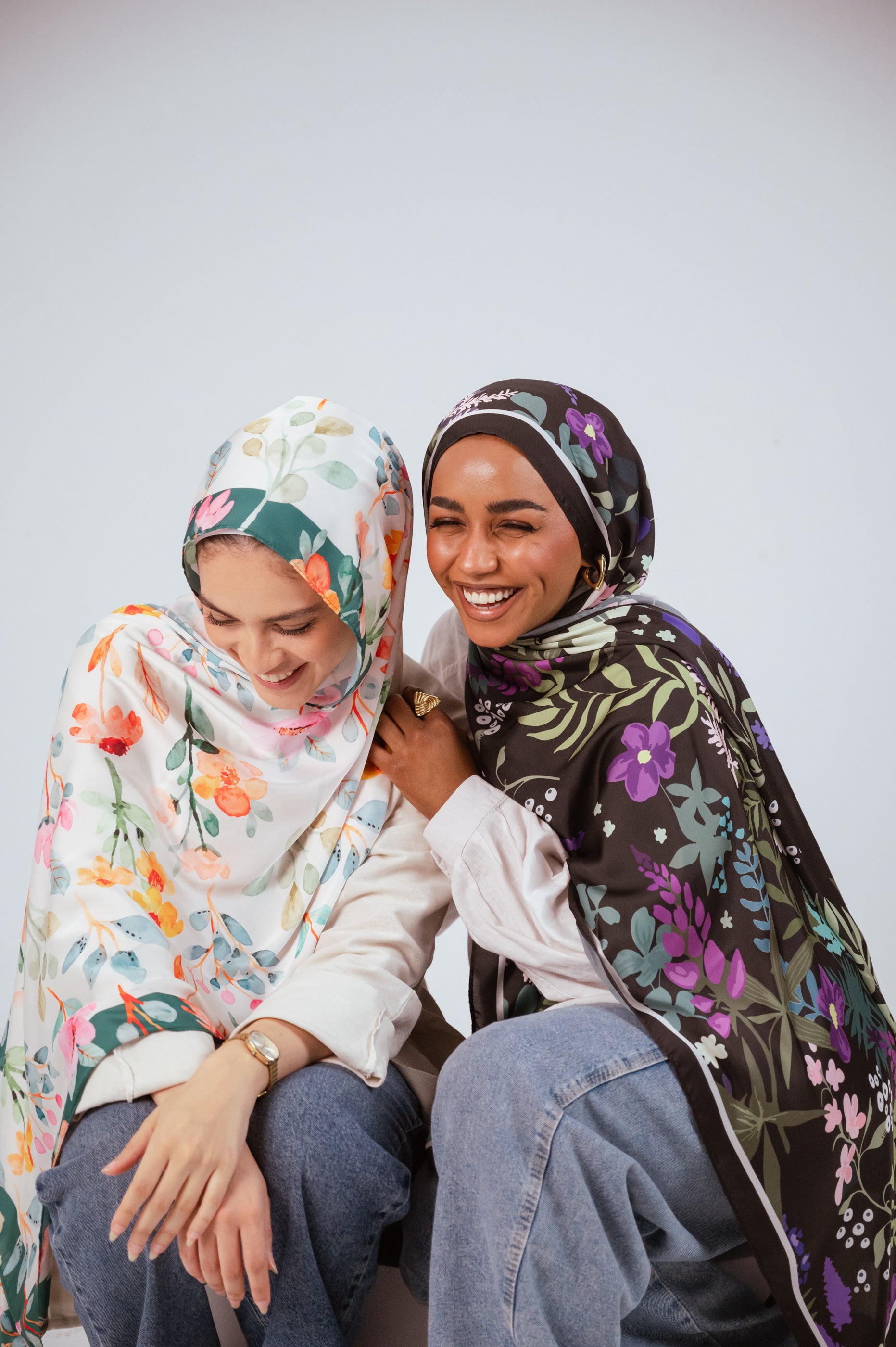 Two models in the Andalus Drape and Blooms of Hope satin hijabs sharing a candid moment, smiling and looking down.
