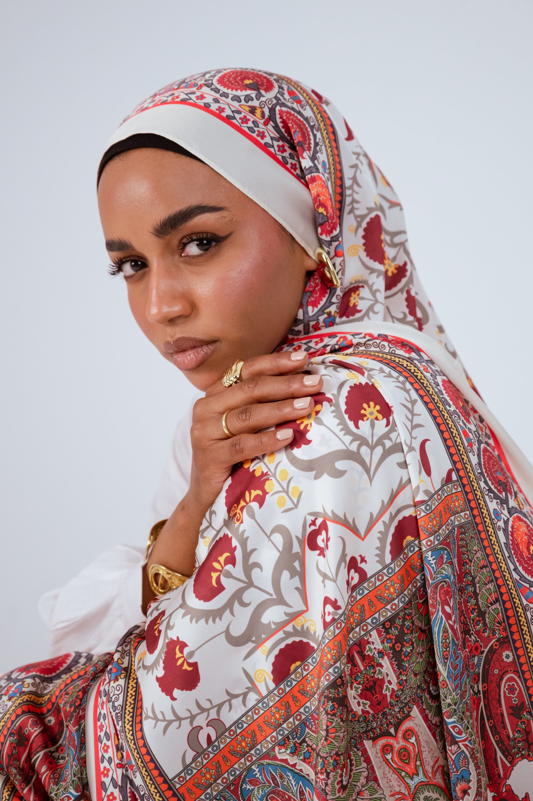 Soft gaze portrait of model wearing the Cairo Nights Satin Hijab, showcasing the cream base and bold red detailing.