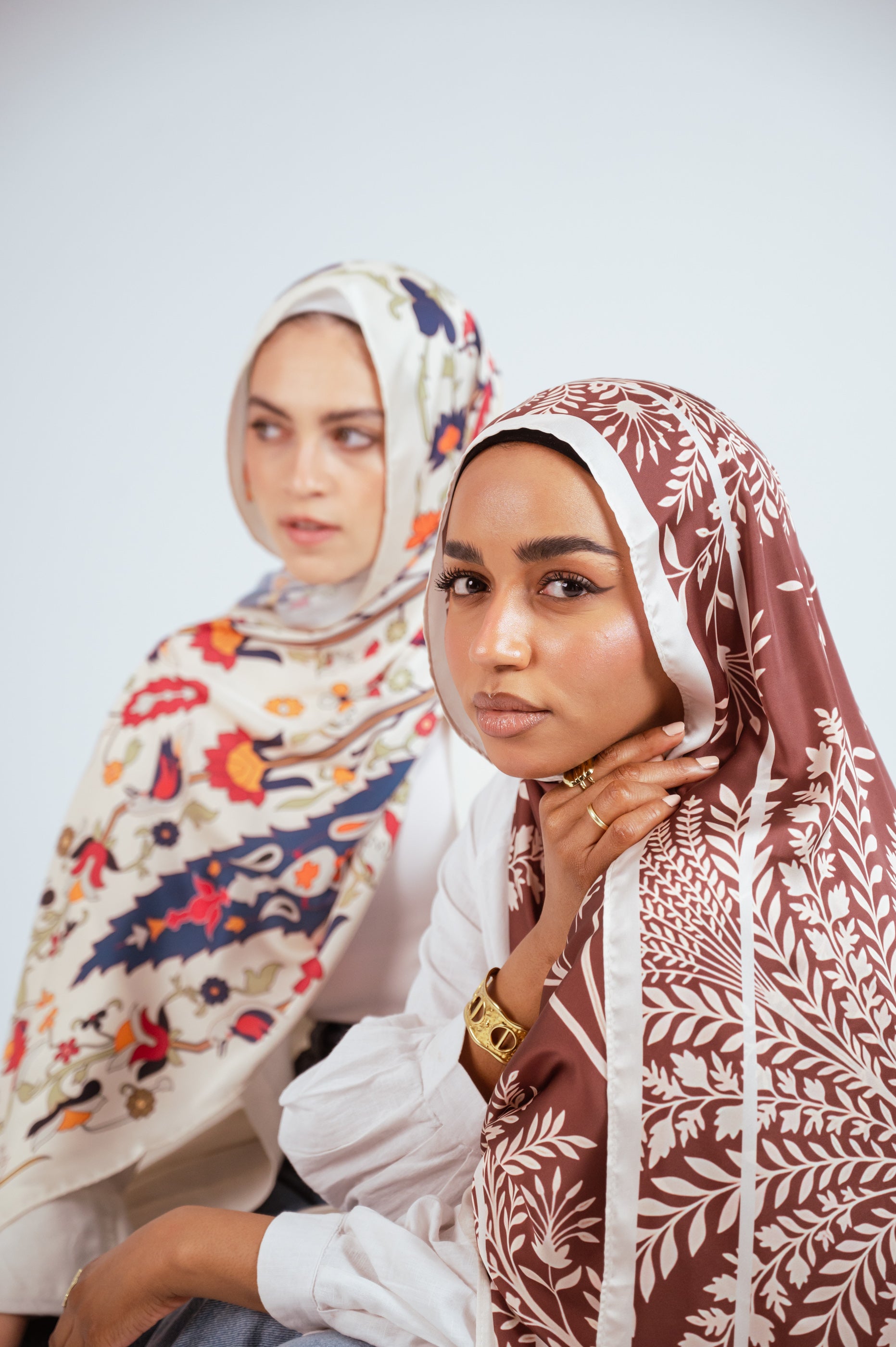 Close-up of two women wearing Andalus Drape Satin and Rose of Petra Satin hijabs, highlighting the printed satin details.