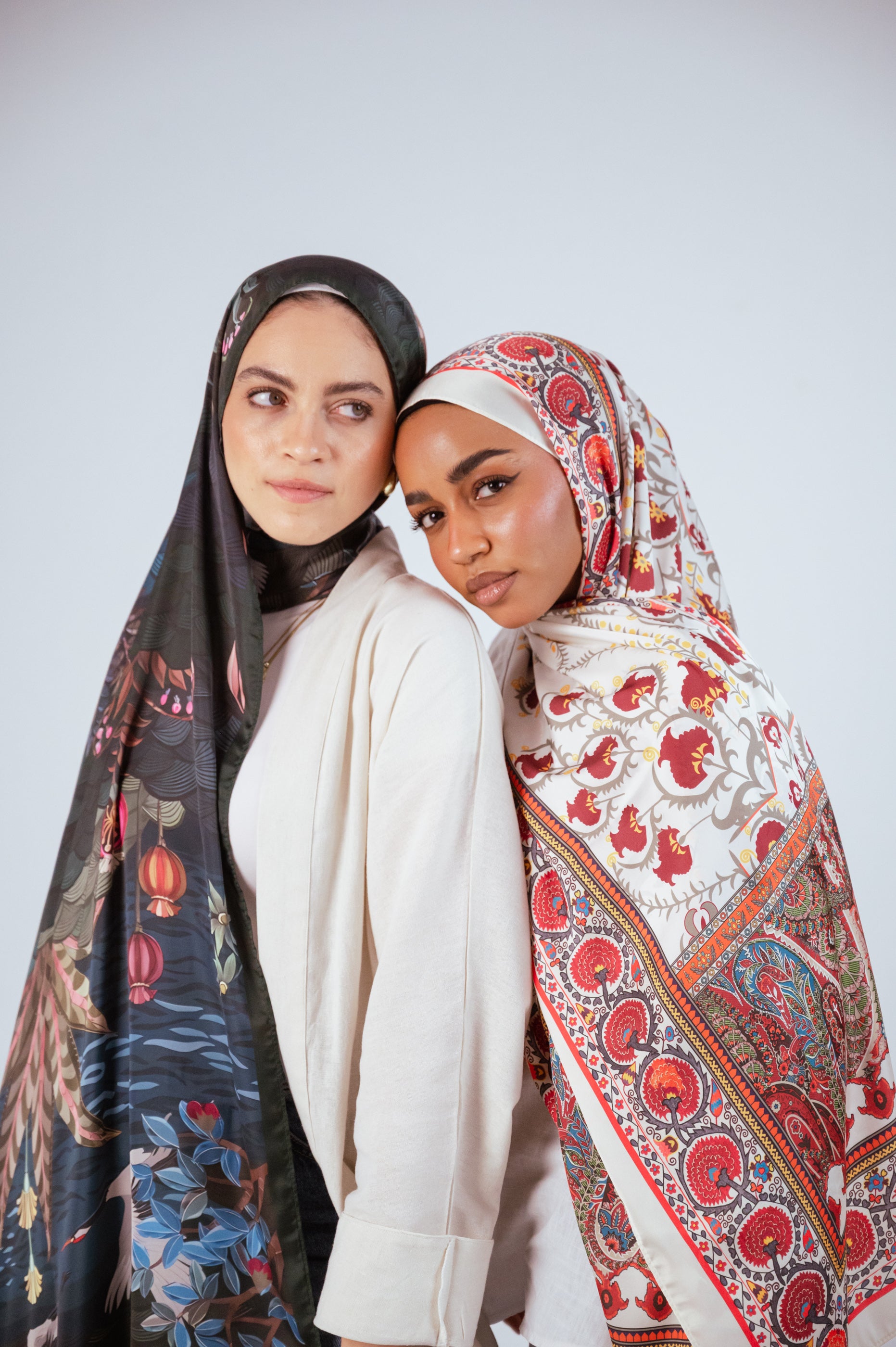 Two models wearing JAIDA’s Cairo Nights Satin Hijab and Secret Garden Chiffon Hijab standing side-by-side, showcasing the contrast between bold red motifs and deep botanical prints.