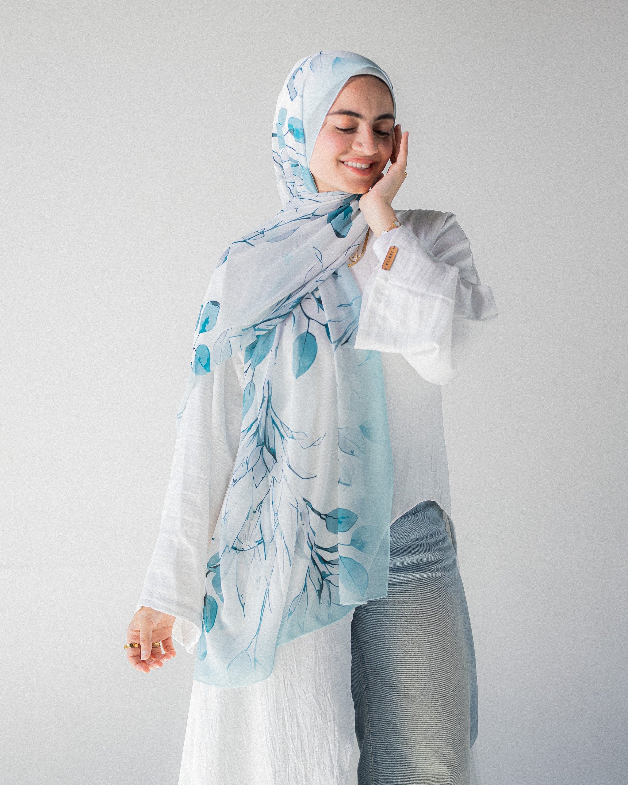 Modest Muslim young woman wearing a light blue hijab with floral patterns on a plain background