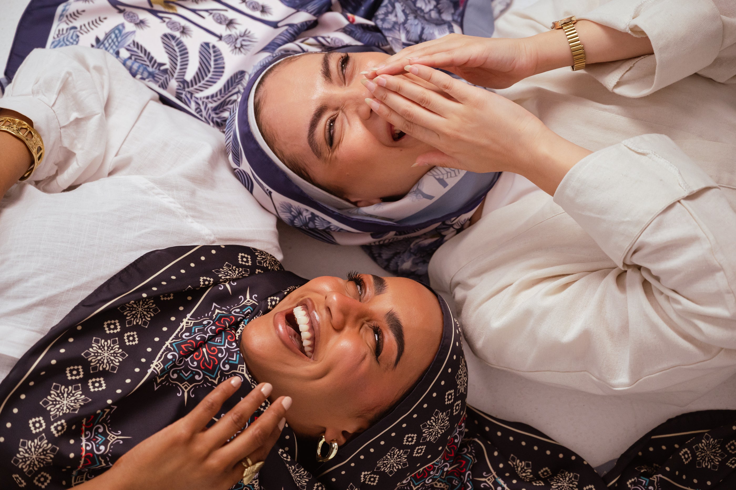 Two women smiling in an editorial lifestyle photo wearing art-inspired hijabs by Jaida — premium & luxury modest fashion designed in Canada.