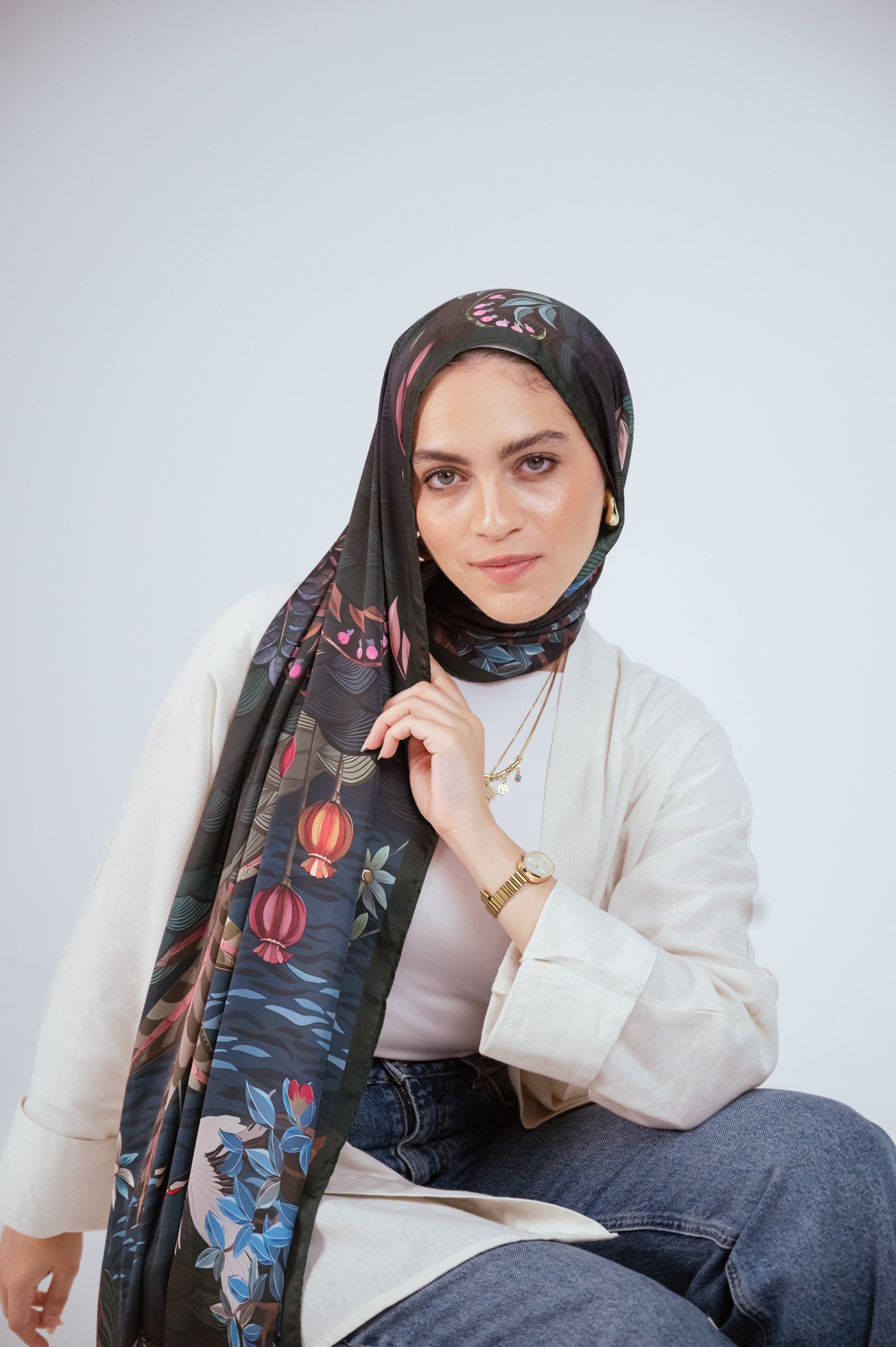 Seated pose, model holding hijab showing lantern-like botanical motifs.