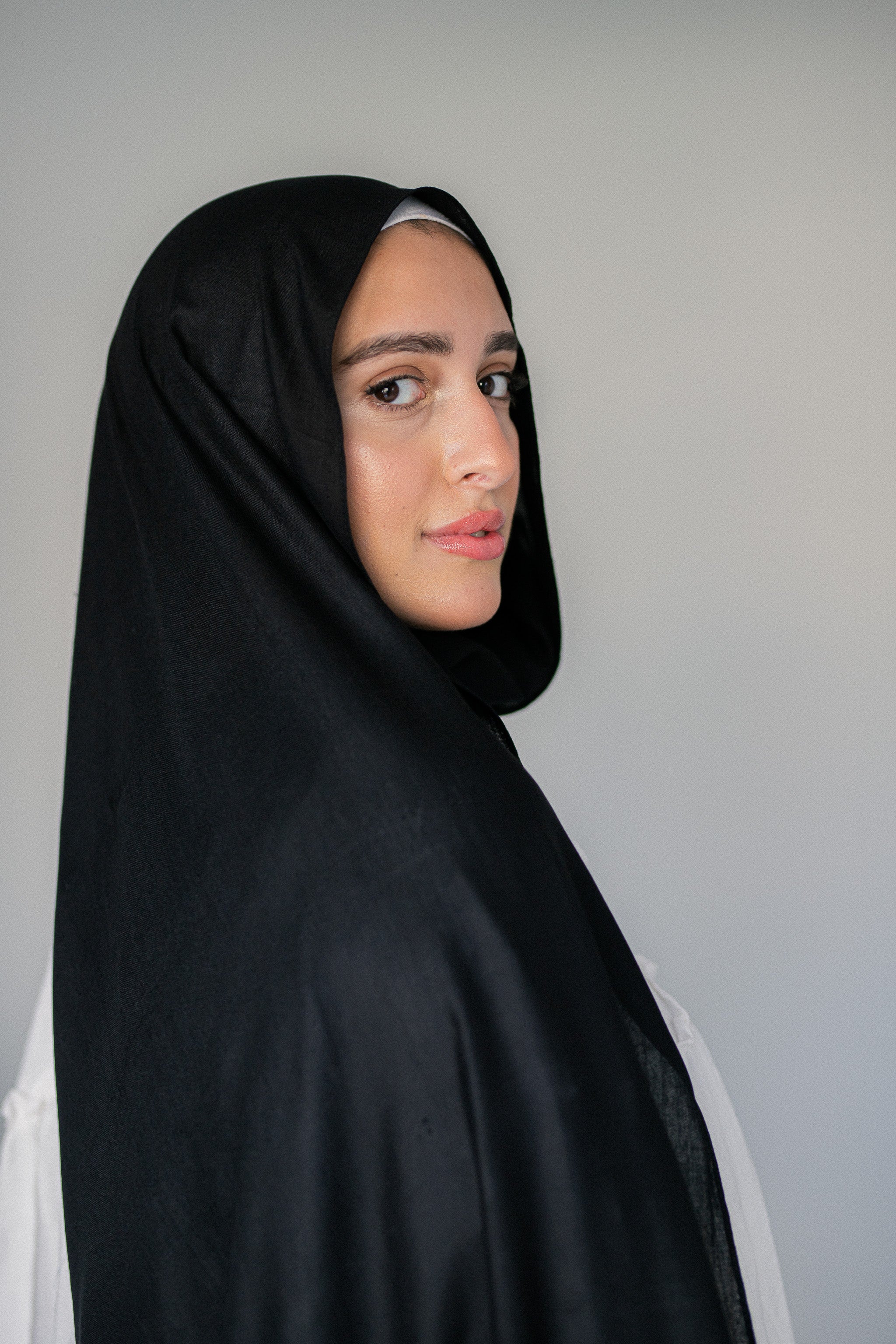 Woman wearing Jaida’s Noir Éclipse black modal cotton hijab styled simply with a white blouse, showing elegant drape and natural texture.