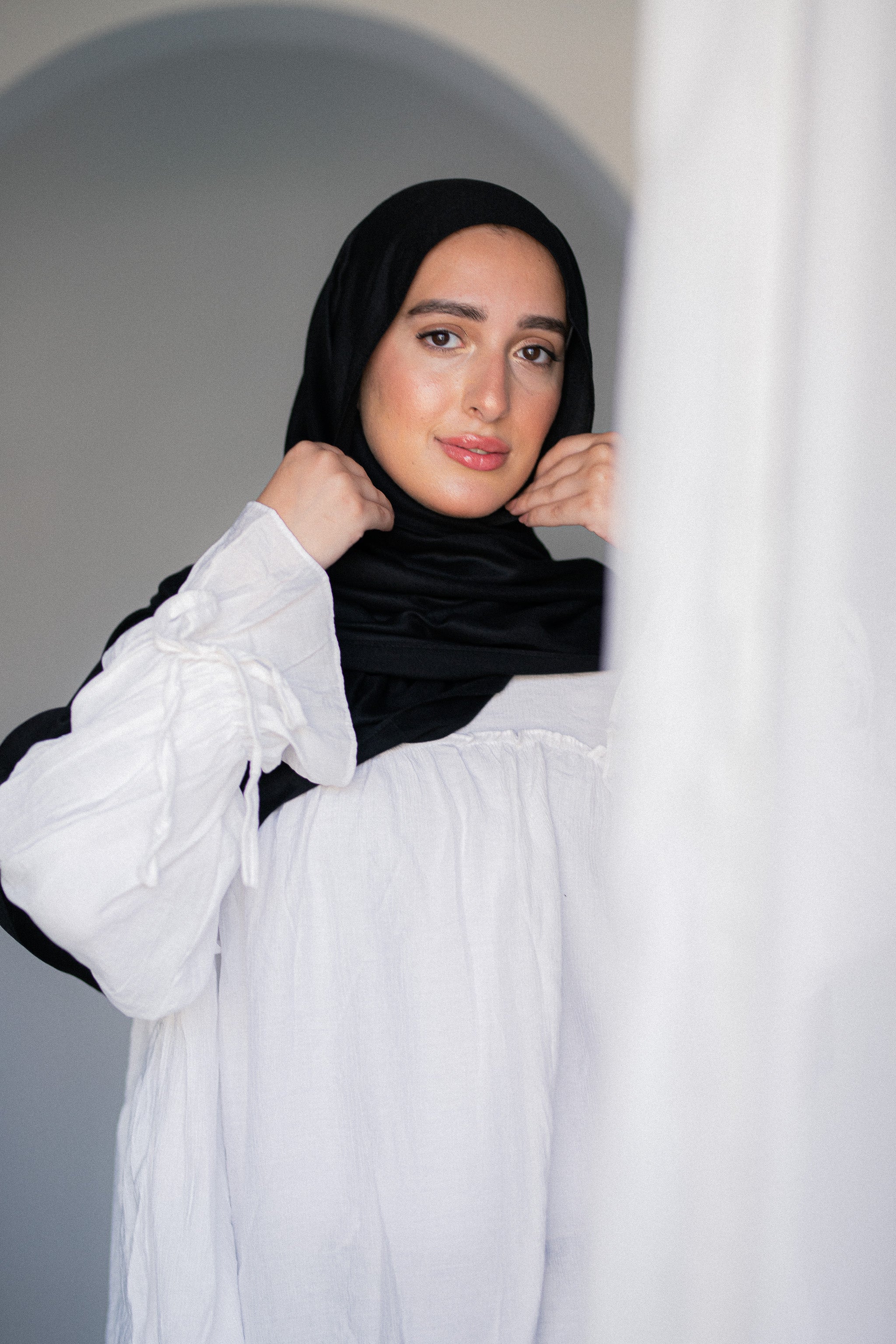 Woman wearing Jaida’s Noir Éclipse black modal cotton hijab styled simply with a white blouse, showing elegant drape and natural texture.