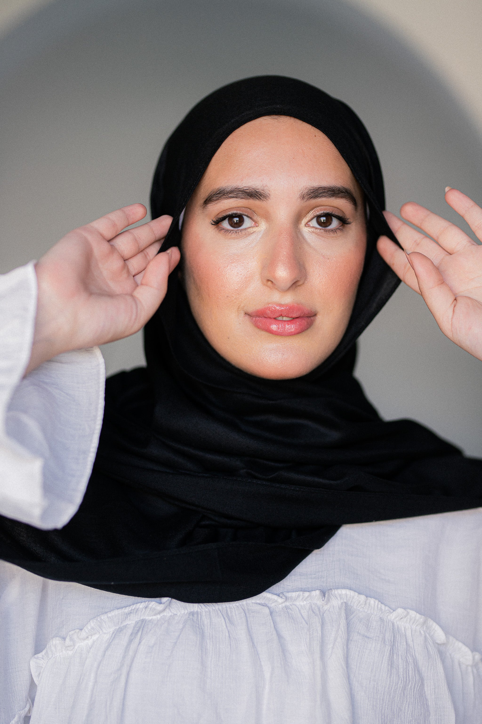 Close-up of model adjusting Noir Éclipse black hijab, highlighting its soft modal cotton texture and elegant fall.