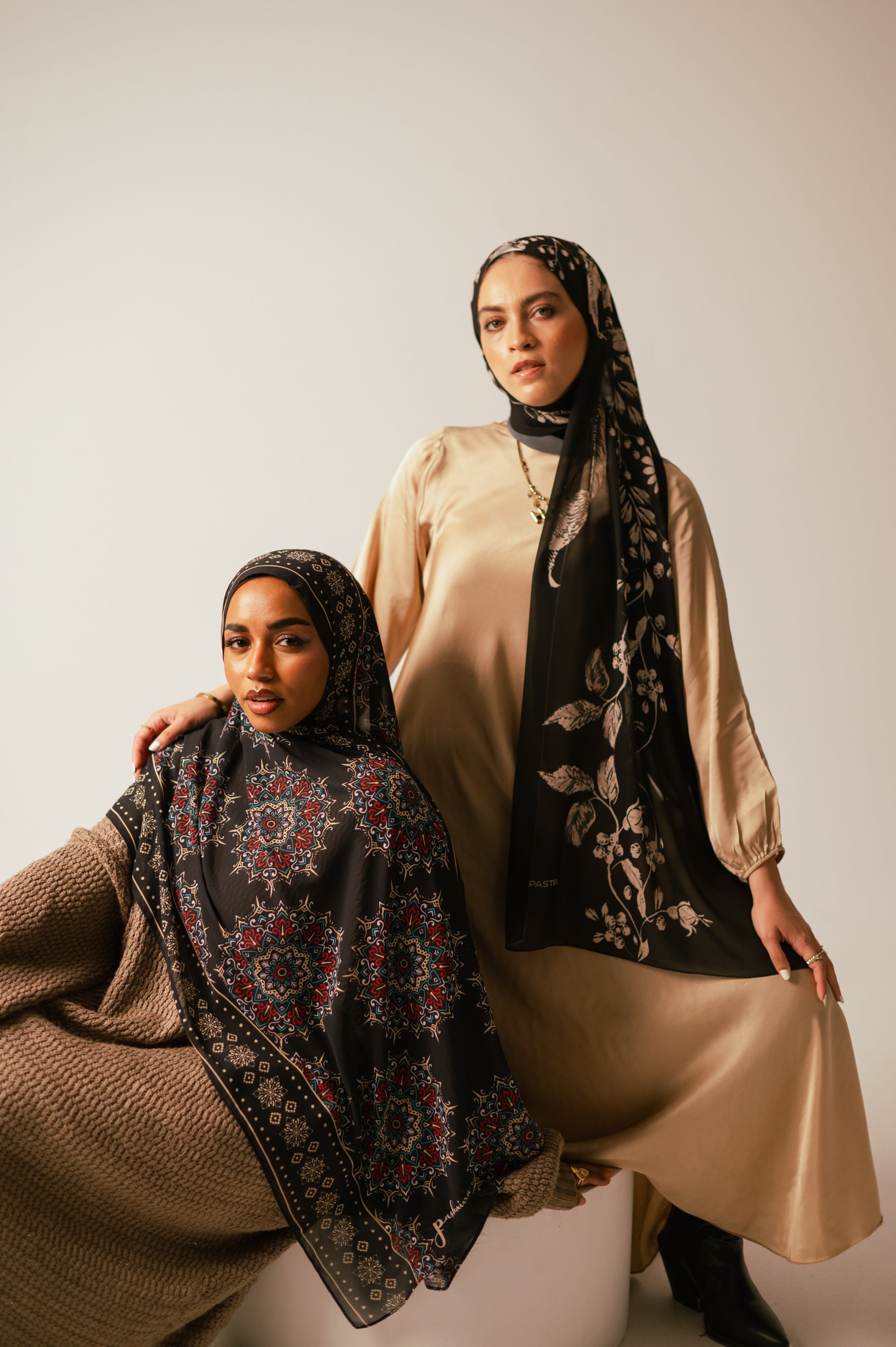 Two models wearing Petal Shadows chiffon hijab and a mandala-print chiffon hijab in a standing portrait pose, highlighting the fabric flow and intricate prints.