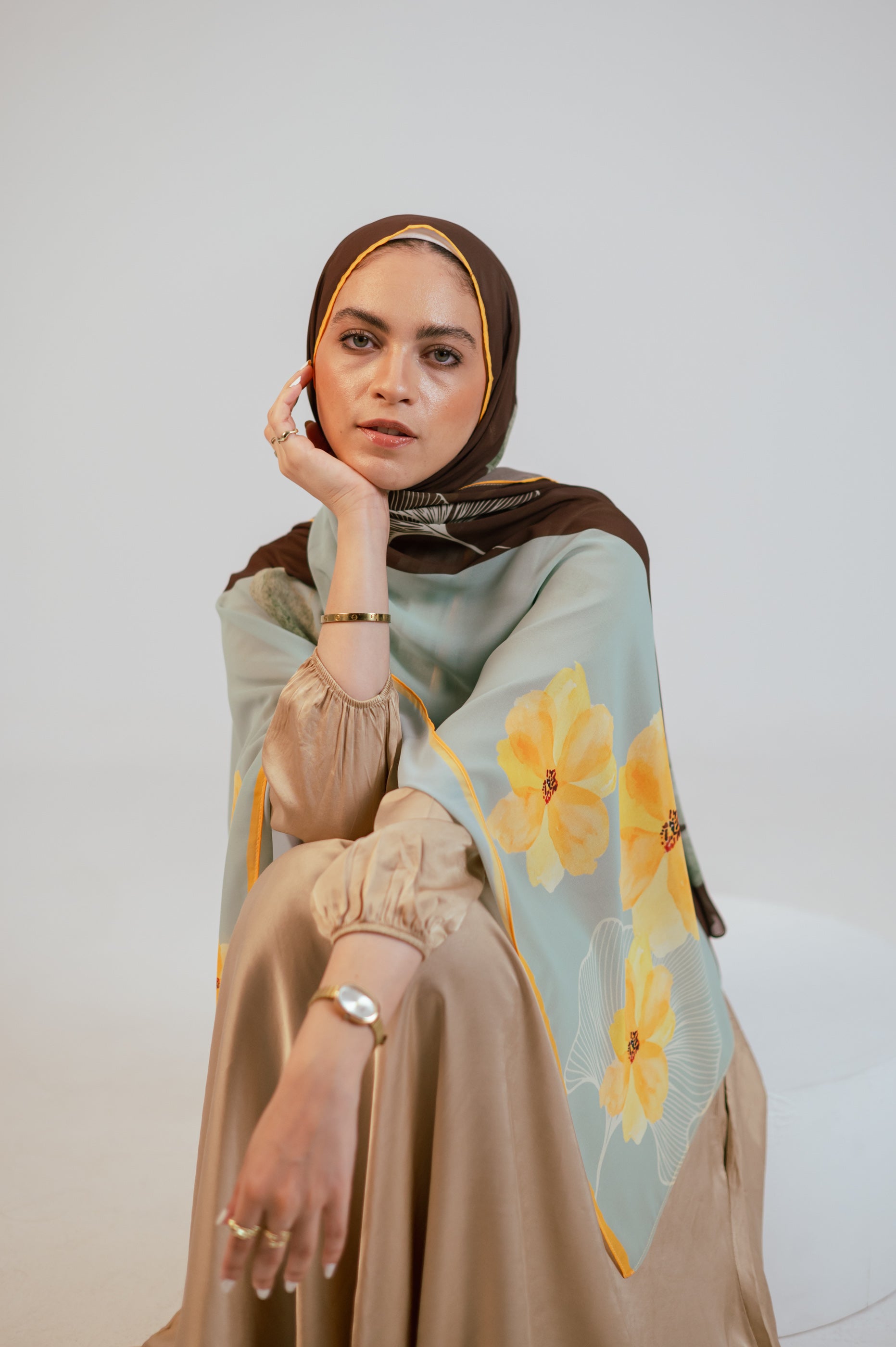 Front seated pose of the model showcasing the Terra Soleil luxury chiffon hijab, featuring its airy drape and soft floral artwork.