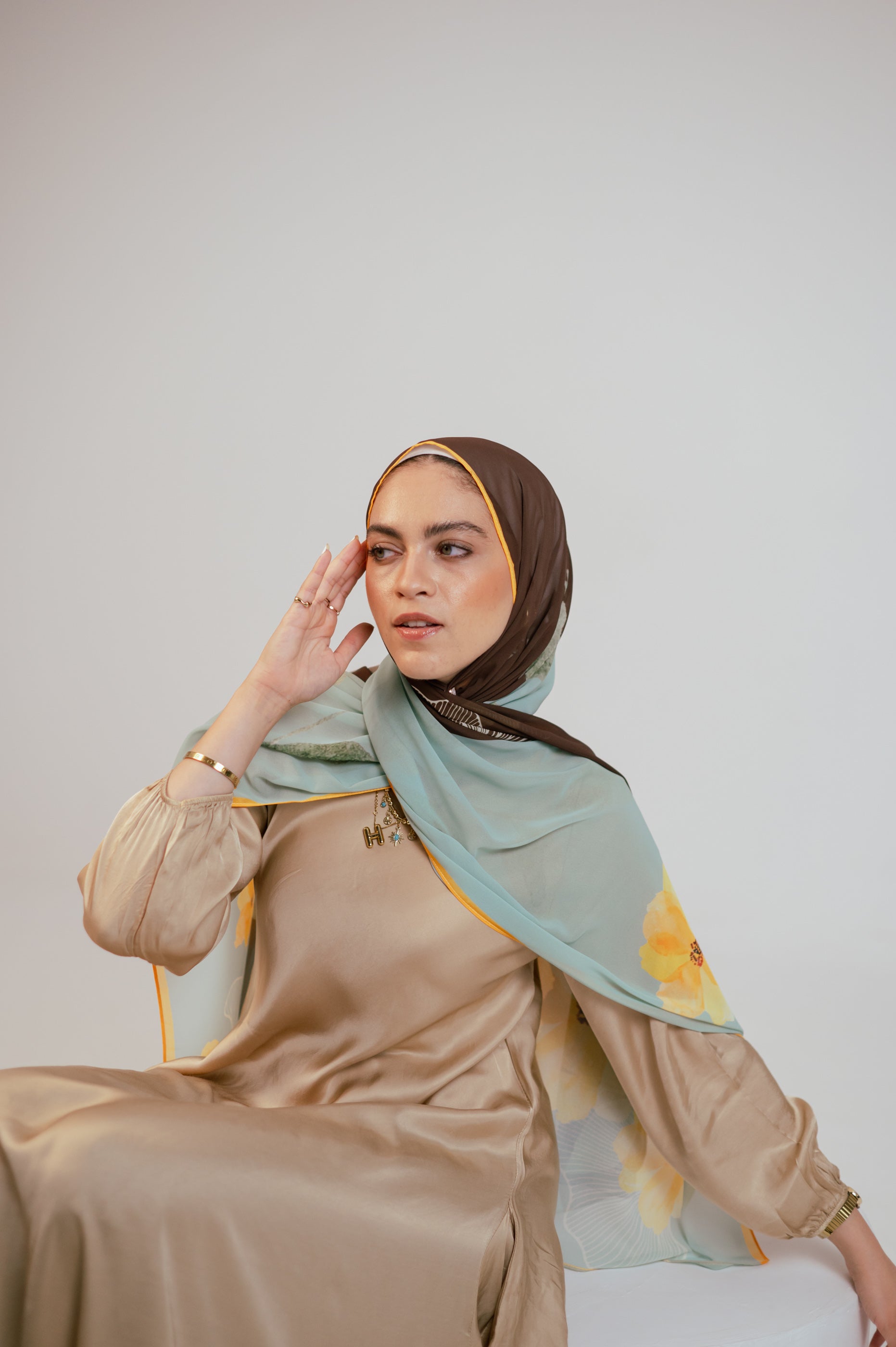 Close-up of the Terra Soleil chiffon hijab with the model touching her face, highlighting the contrast brown border and soft floral print.